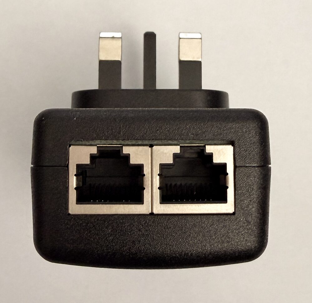 The included PoE injector, a black UK three-pin plug with two ethernet sockets